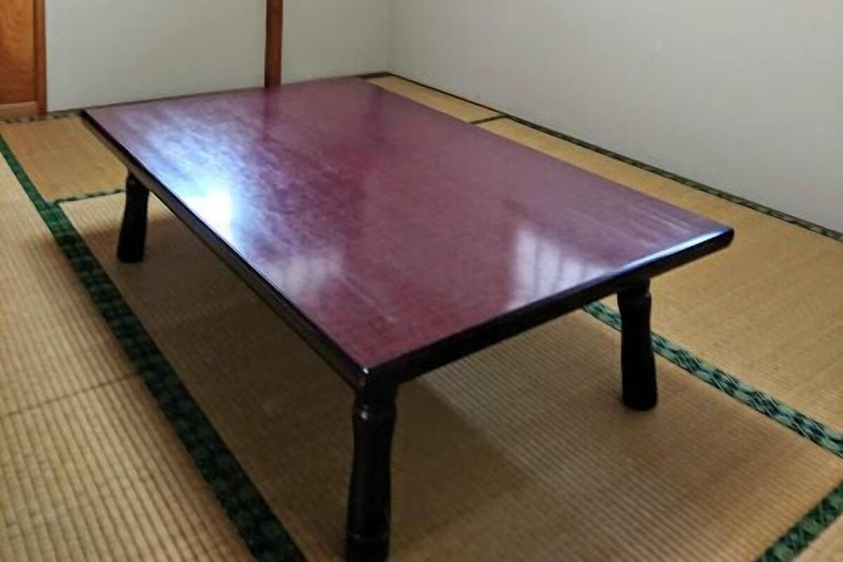 A room with tatami mat flooring, a wooden table, a television on a shelf, and a clock on the wall.