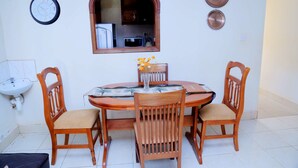 A dining area with a round table, four wooden chairs, a vase with flowers, a wall clock, a mirror, and two decorative plates. - Floben Apartments (Kampala)
