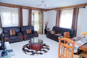 Una sala de estar moderna con dos sofás de cuero negro, una mesa de centro de vidrio, una mesa de comedor de madera con sillas y un jarrón decorativo con flores.