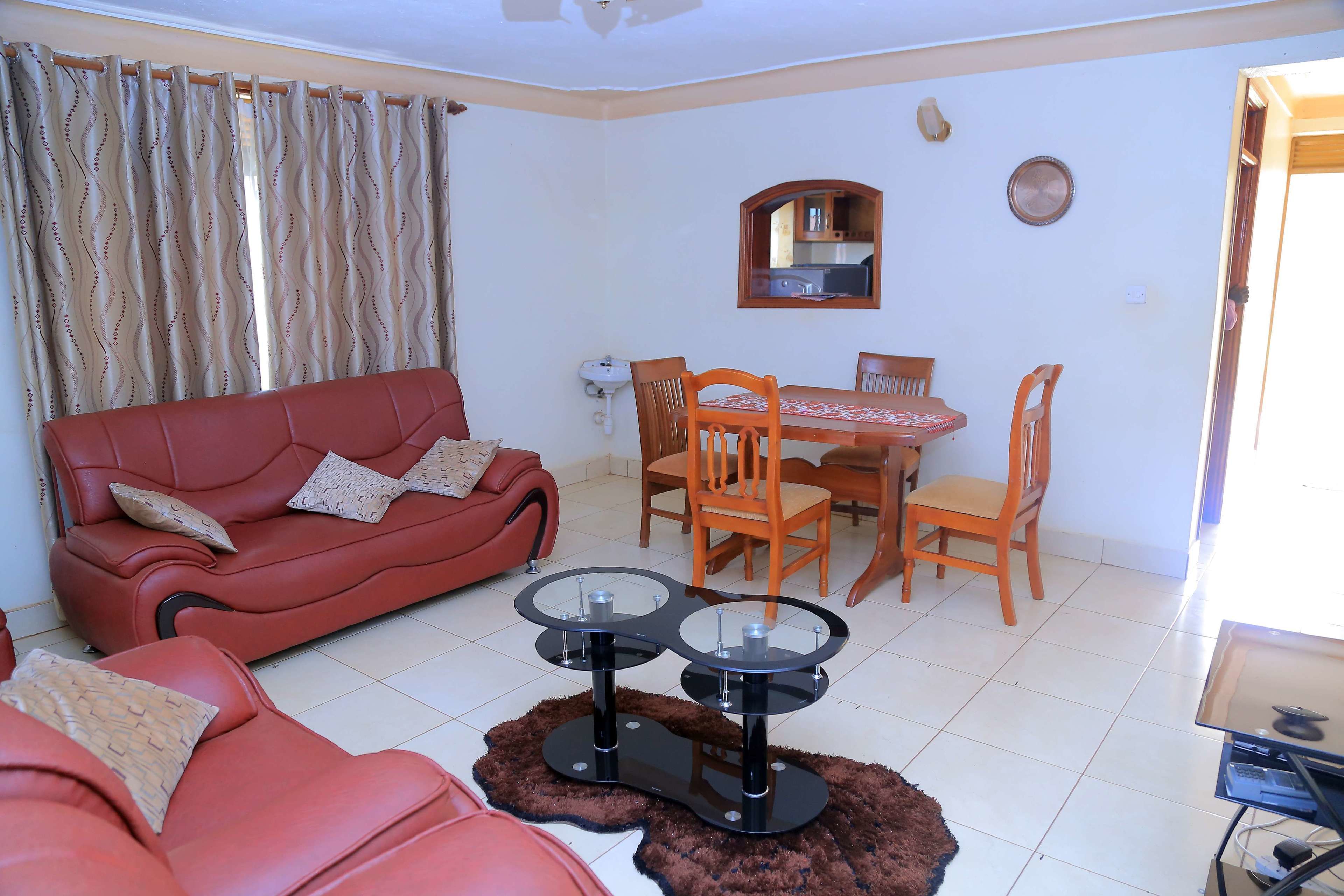 Un salon avec un canapé rouge, une table à manger entourée de chaises et un petit coin cuisine visible à travers une porte ouverte.