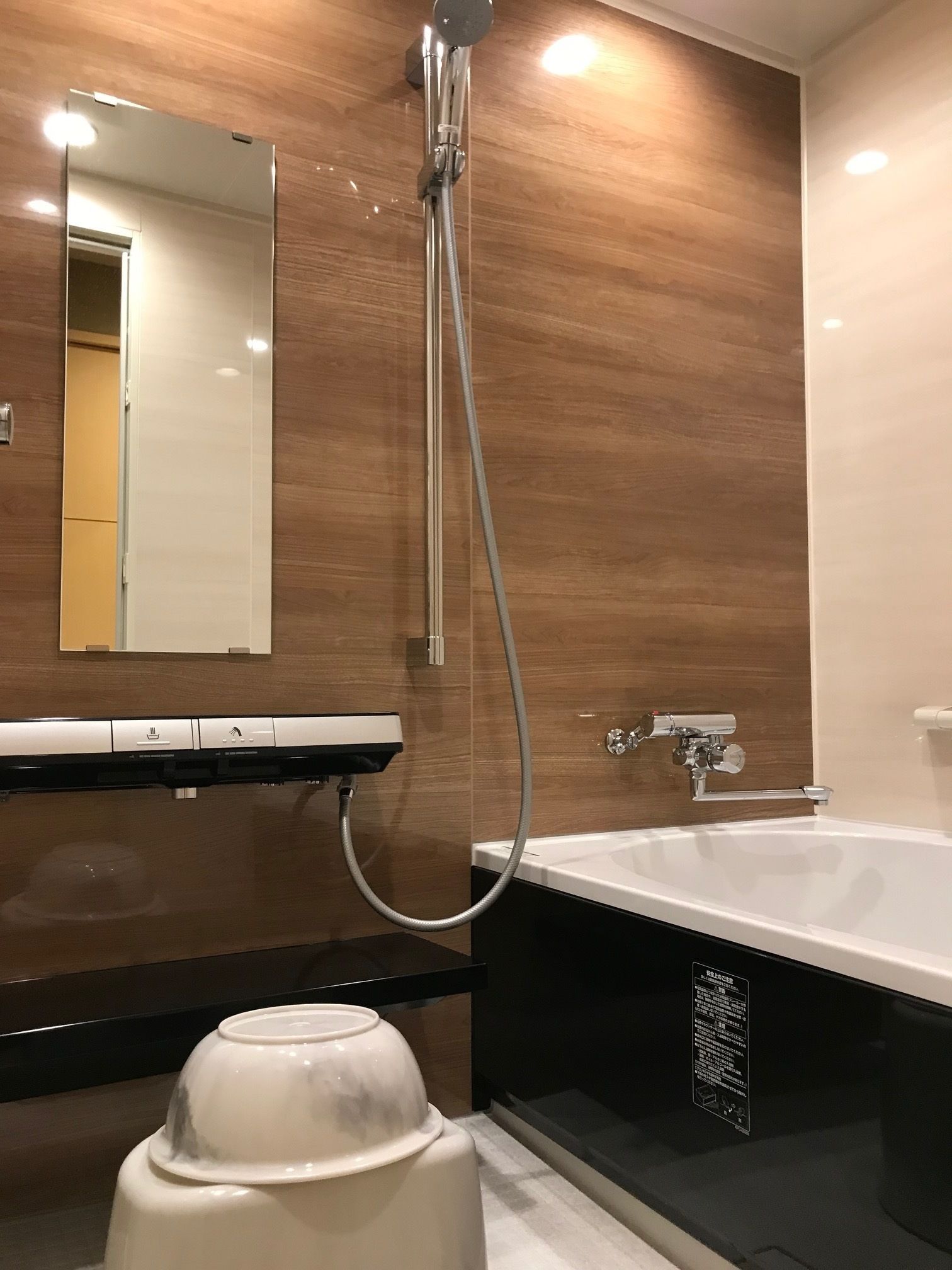 Un baño moderno con pared de madera, un espejo grande, una bañera y un lavabo pedestal blanco.