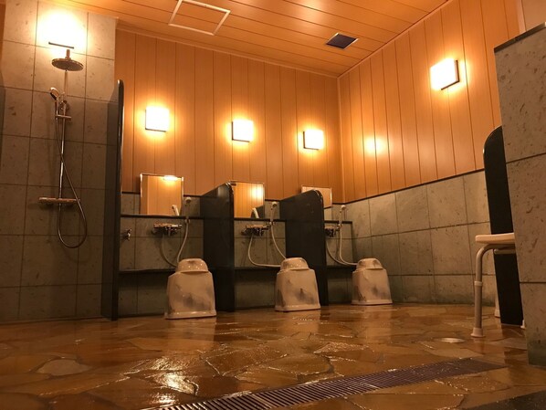 A public restroom with wooden panel walls, multiple urinals, and a shower area.