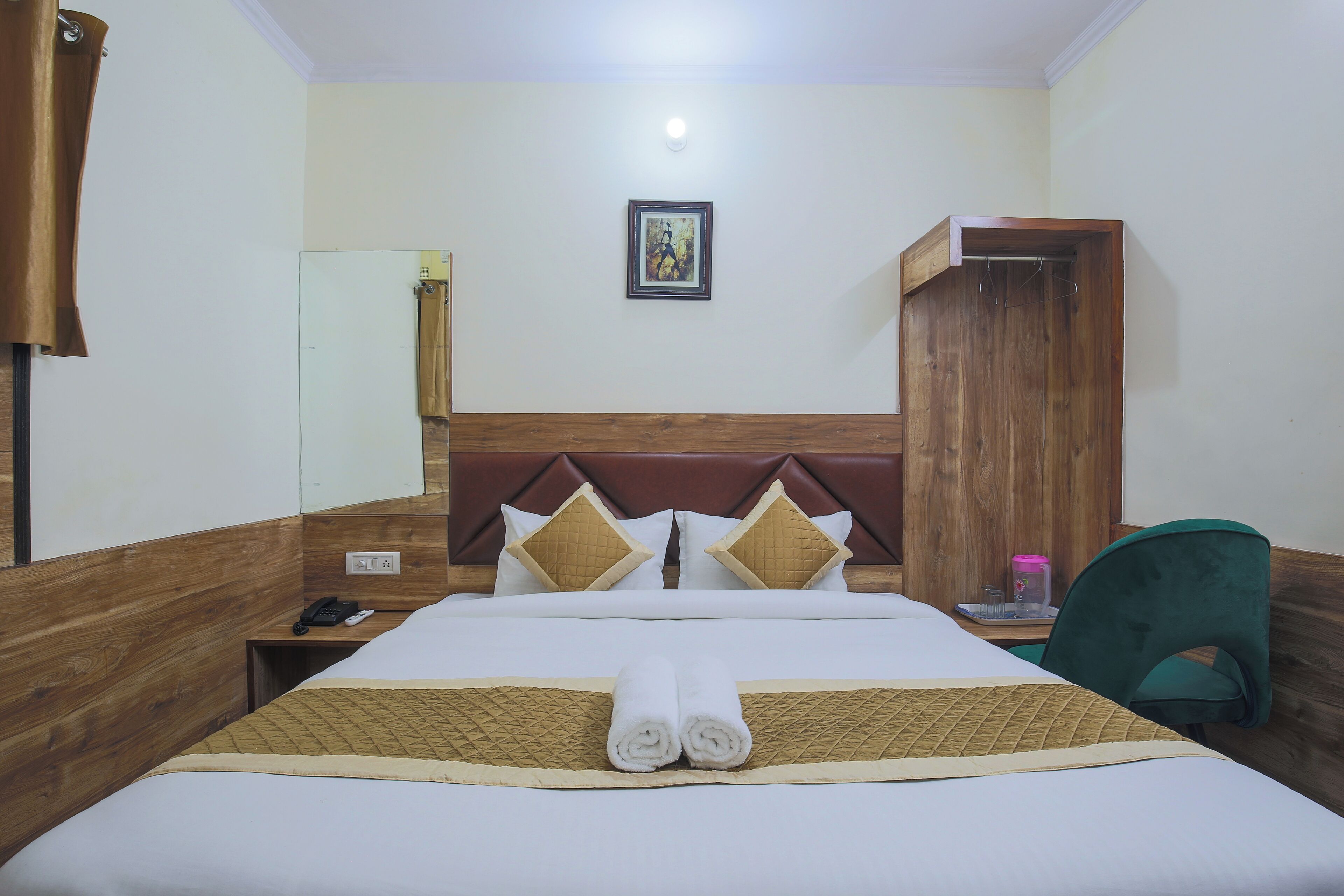 A hotel room with a wooden headboard, a bed with white linens, two pillows, a bedside table with a phone, and a green chair.