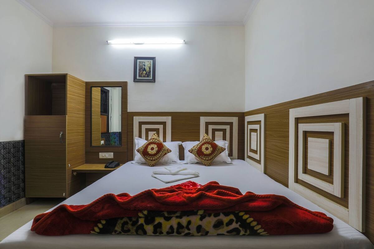 A hotel room with a bed, a wardrobe, a mirror, and a framed picture on the wall.