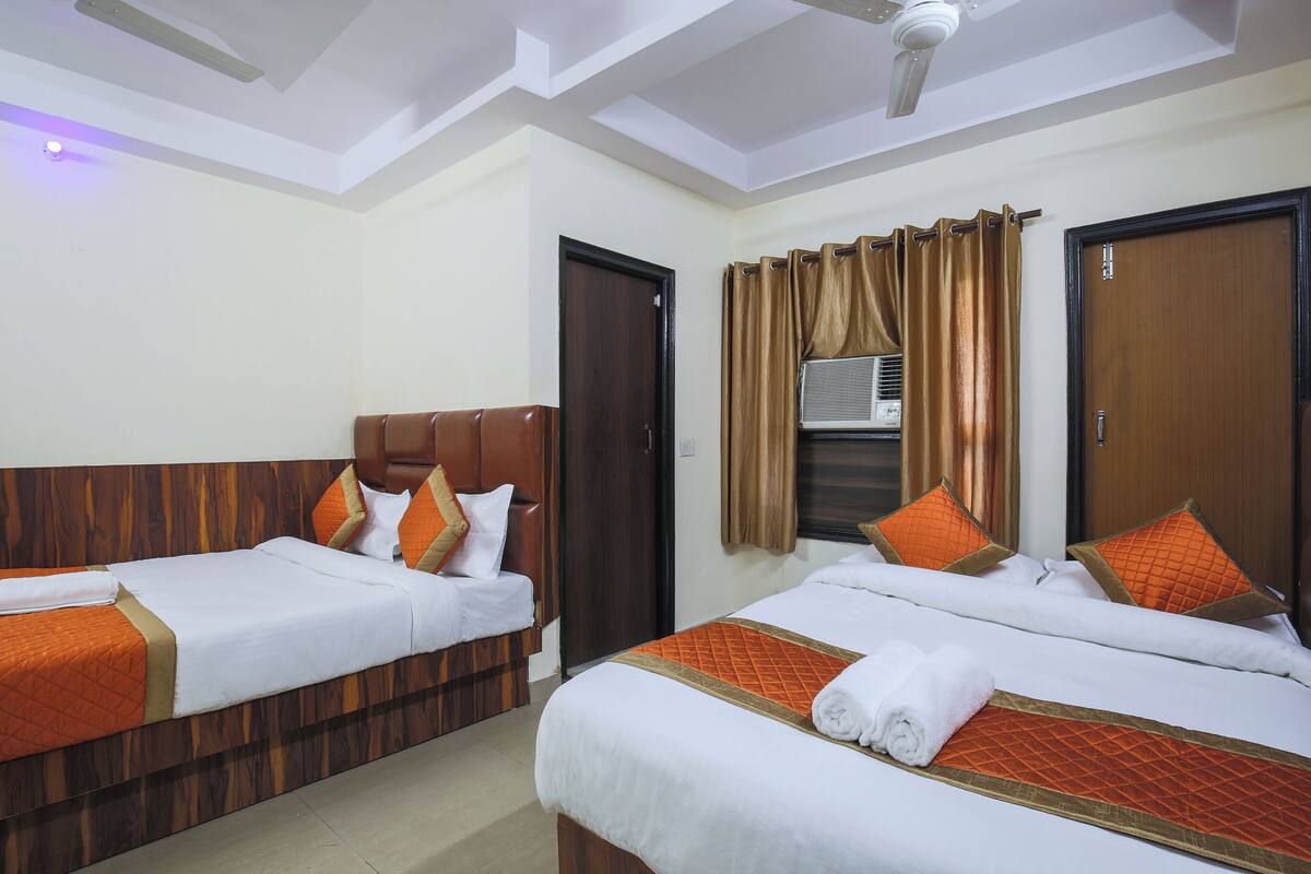 A hotel room with two beds, each with a wooden headboard, white bedding, and orange accents. There is a ceiling fan and a window with curtains.