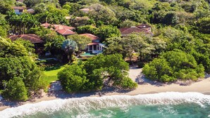 Vista aérea de uma propriedade costeira com várias casas, uma praia e uma piscina.