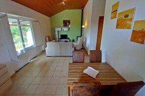 A spacious living area with a wooden ceiling, a dining table with chairs, a sofa, and a TV.
