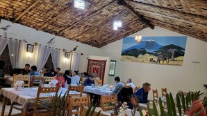 Un restaurante con mesas y sillas de madera, techo de paja y un mural de fauna en la pared.