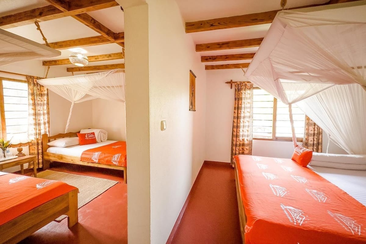 A room with two beds, each with a canopy, wooden beams on the ceiling, and a window with curtains.