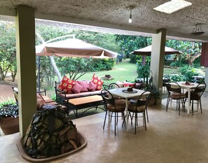 A covered patio area with a table and chairs, a cushioned bench with pillows, and a stone fountain.