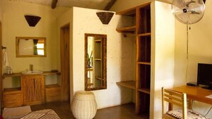 A room with a wooden bed, a small bedside table, a mirror, a wooden cabinet, a fan, and a desk with a chair. - Gately Inn Entebbe (Entebbe)