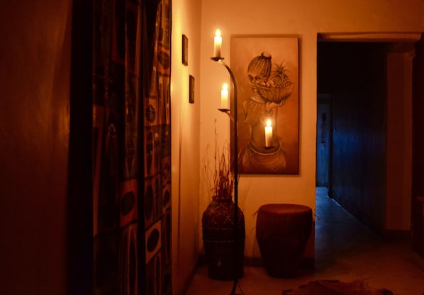 A dimly lit hallway with a decorative vase, a candle holder, and a framed artwork on the wall.