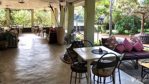 An indoor seating area with tables and chairs, a large vase, and a view of a garden through large windows. - Gately Inn Entebbe (Entebbe)