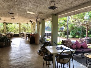 An indoor seating area with tables and chairs, a large vase, and a view of a garden through large windows.
