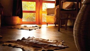 A room with a wooden floor, two woven chairs, a woven basket, and a woven rug. - Gately Inn Entebbe (Entebbe)