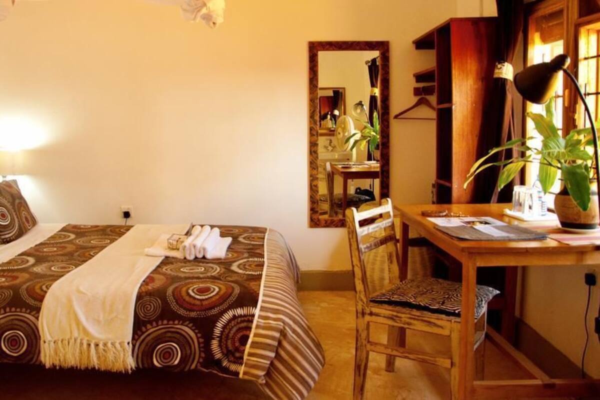 Un dormitorio ordenado con cama, mesita de noche, silla y espejo.