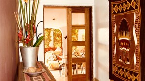A room with a wooden table, a potted plant, a traditional tapestry, and a view of a cozy sitting area with a sofa and chairs. - Gately Inn Entebbe (Entebbe)
