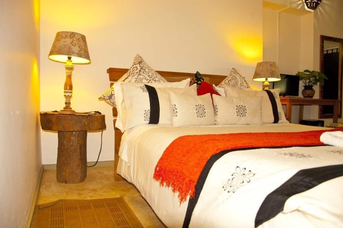 Una cama bien hecha con una manta blanca y roja, dos lámparas de noche y almohadas estampadas.