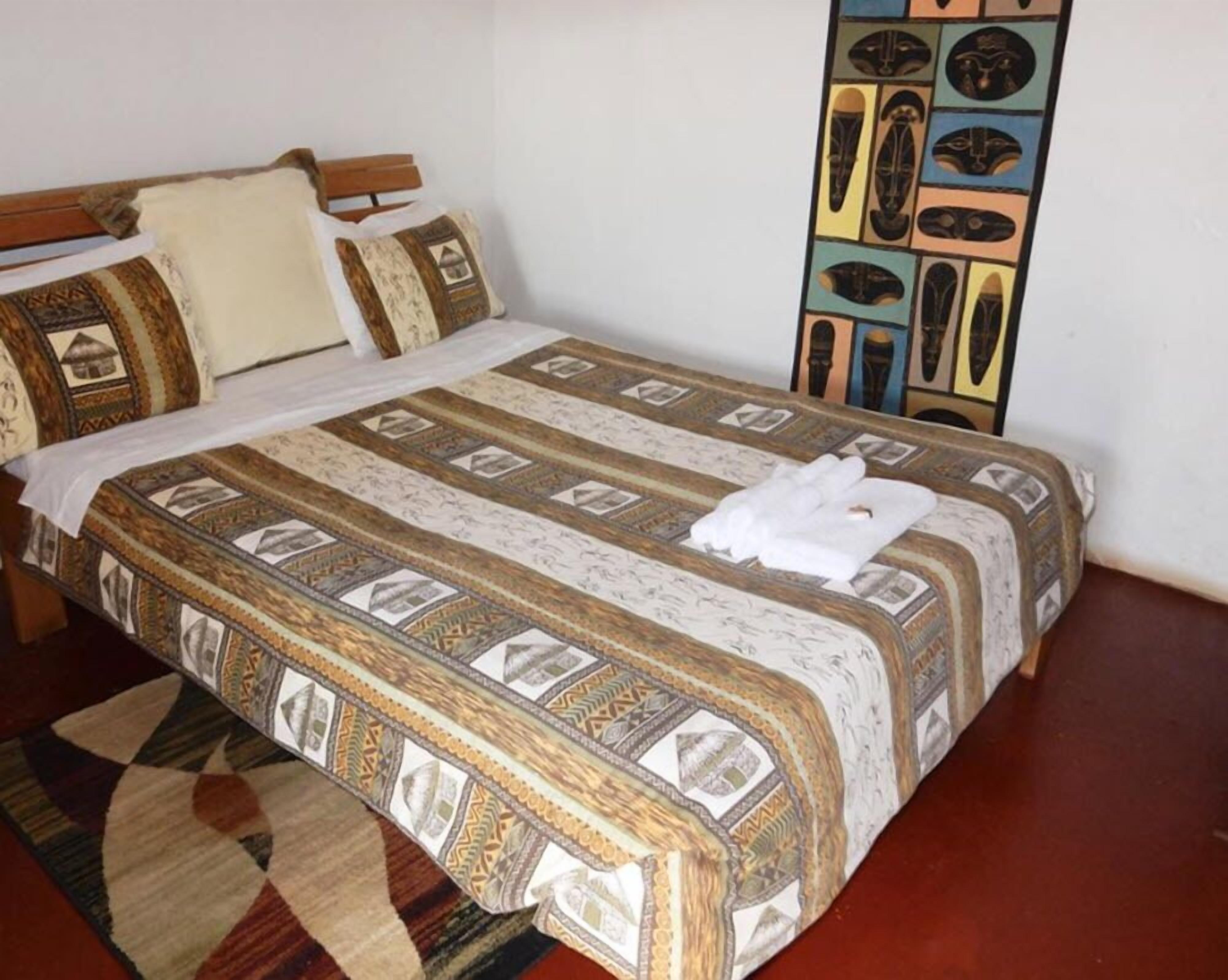 A neatly made bed with a patterned bedspread and pillows, a wooden headboard, and a decorative wall panel.