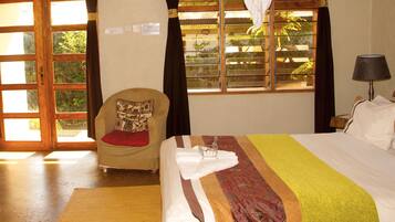 Una habitación de hotel con cama, una silla, ventana y vistas a zonas verdes, además de una lámpara.