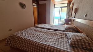 A bedroom with two beds, a wooden headboard, a small wall decoration, and a view of the outside. - Albufeira Sea view (51) (Albufeira)