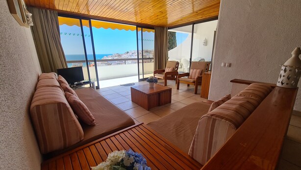 A spacious living area with a wooden ceiling, large sliding glass doors leading to a balcony, a sofa set, a coffee table, and a television. - Albufeira Sea view (51) (Albufeira)