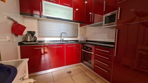 A compact kitchen with red cabinets, a microwave, and a sink. - Albufeira Sea view (51) (Albufeira)