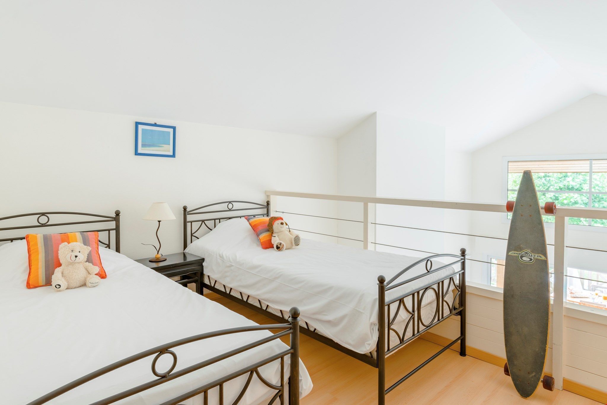 Une chambre avec deux lits, une table de chevet, une lampe, un ours en peluche et une planche de surf.