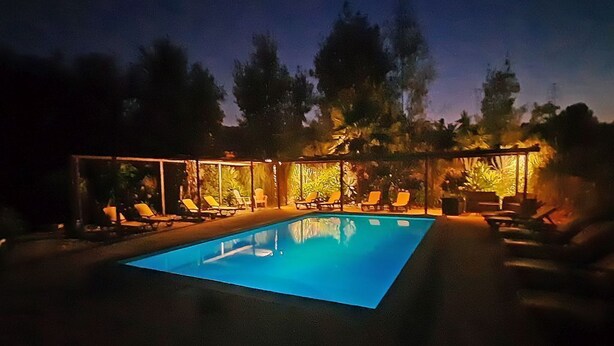 Una piscina con sillas de descanso y una zona cubierta, rodeada de árboles.