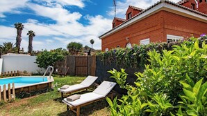 A backyard with a swimming pool, two lounge chairs, and a brick house with a tiled roof. - GC0181 Holiday cottage in Valsequillo (Valsequillo)