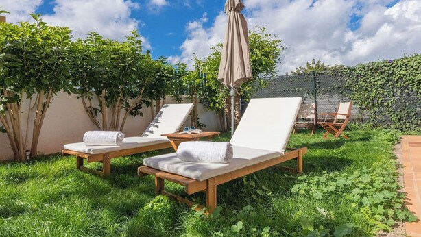 A garden area with two wooden lounge chairs, a table with a towel, and a large umbrella. - GC0181 Holiday cottage in Valsequillo (Valsequillo)