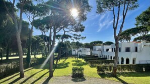 Un cortile con siepi curate, un vialetto e edifici bianchi con finestre ad arco.