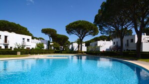 Una piscina circondata da edifici bianchi con balconi, alberi e un cielo sereno.