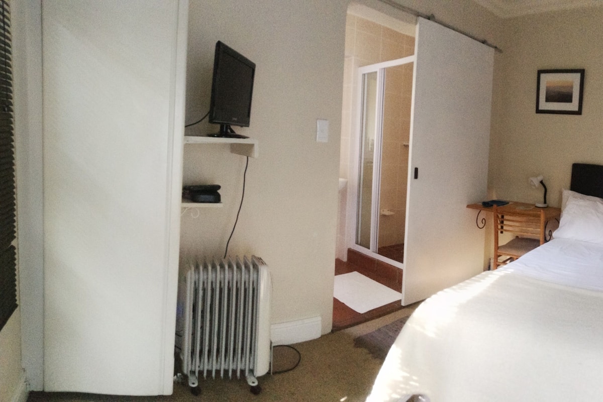 A hotel room with a bed, a television on a shelf, a radiator, and a door leading to a hallway.