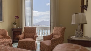 Une chambre d’hôtel avec une grande fenêtre, deux fauteuils à motifs, une petite table avec une lampe et une statue décorative.