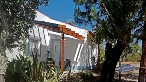 Un edificio blanco con una pérgola de madera, rodeado de plantas y árboles.