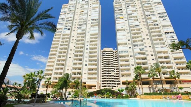Un hotel moderno de gran altura con varios balcones, una piscina y palmeras.