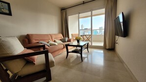 A living room with a sofa, armchair, coffee table, and a TV mounted on the wall. - Gemelos 22 Apartments (Benidorm)
