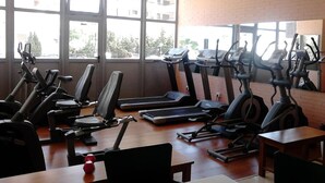 A gym with multiple treadmills and stationary bikes, large windows, and a brick wall. - Gemelos 22 Apartments (Benidorm)