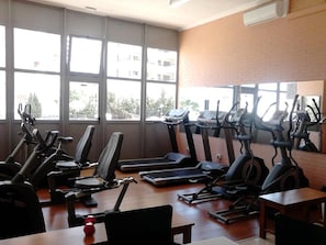 Une salle de sport équipée de plusieurs tapis de course et de vélos d’appartement, dotée de grandes fenêtres et d’un mur en briques.