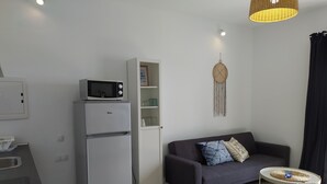 A compact living space with a kitchenette, a gray sofa, a small round table, and a decorative wall hanging. - QUINTERO SUITES (NOPAL AND VEROL) 2 COUPLES? BOOK THE TWO SUITES (San Bartolomé)