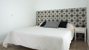 A neatly made bed with a white bedspread and two pillows, one striped and one solid black, in a room with a star-patterned headboard and a white nightstand with a drawer. - QUINTERO SUITES (NOPAL AND VEROL) 2 COUPLES? BOOK THE TWO SUITES (San Bartolomé)
