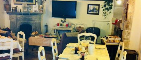 A dining area with tables set for a meal, chairs, a fireplace, and a television on the wall.