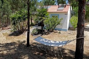 Una casita con techo de tejas, rodeada de árboles y una hamaca.