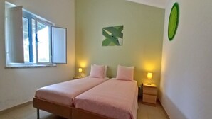 Ein Doppelbett mit zwei Nachttischen, ein Fenster mit Jalousien und einer grünen abstrakten Wanddekoration.