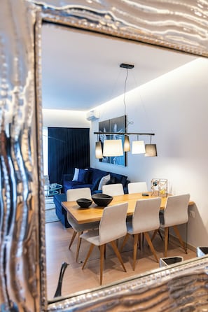 Ein moderner Essbereich mit Holztisch und -stühlen, einer Hängelampe und einem blauen Sofa im Hintergrund.