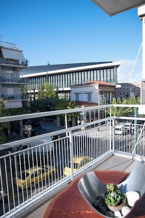 Ein Balkon mit Blick auf eine Straße, ein Gebäude mit rotem Dach und eine Pflanze an der Brüstung.