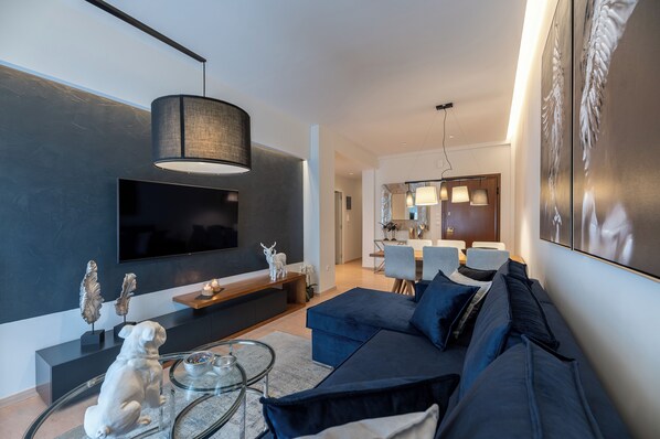 A modern living room with a dark blue sofa, a glass coffee table, and a flat-screen TV mounted on the wall.
