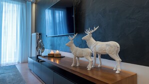 Una sala de estar moderna con una pared oscura con textura, un televisor de pantalla plana grande y dos figuritas de ciervo blanco sobre un mueble de madera.