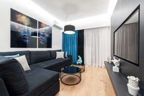 A modern living room with a black sofa, a round coffee table, and a large flat-screen TV.